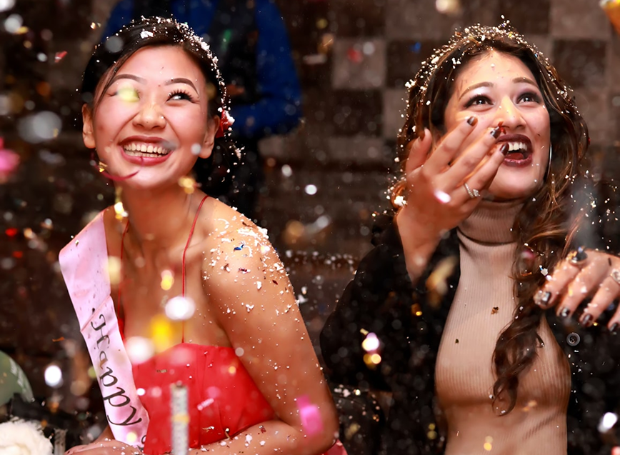 Two friends laughing amid falling confetti