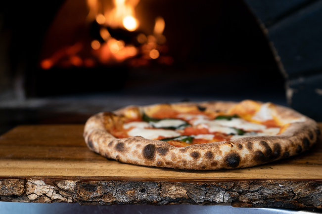 A margherita pizza in front of a glowing wood-fired oven